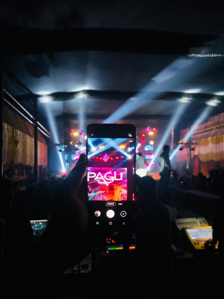 person holding black smartphone taking photo of people in front of stage during night time